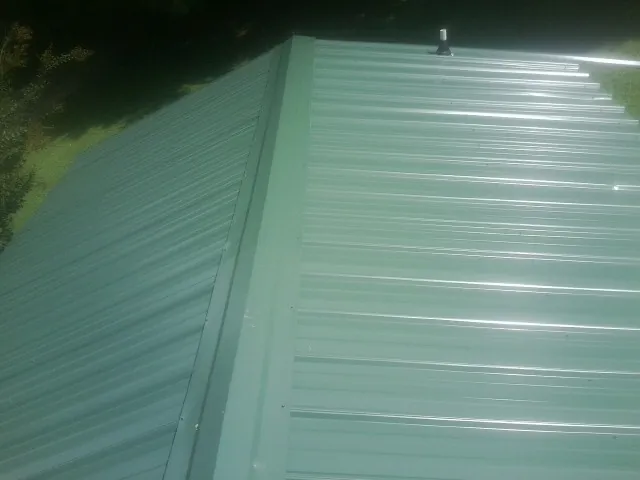 New green metal panels meeting at the ridge of a roof — Flat Roof Repair work by our crew in Fredericksburg