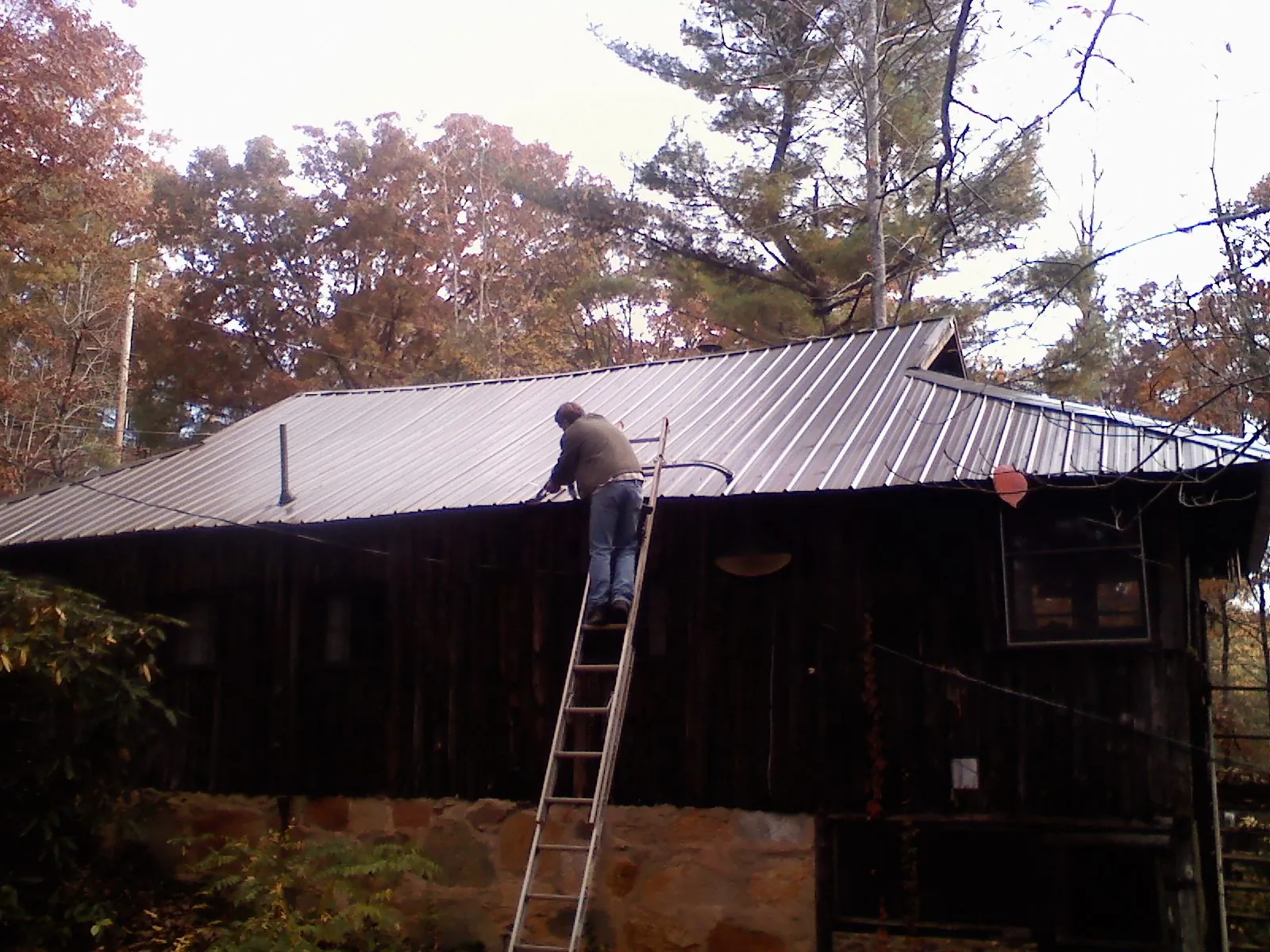 Roofer on a ladder working along the edge of a cabin metal roof in Fredericksburg